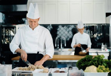 Professional kitchen: two chefs prepare food. The cook cuts mushrooms to prepare delicious dish.