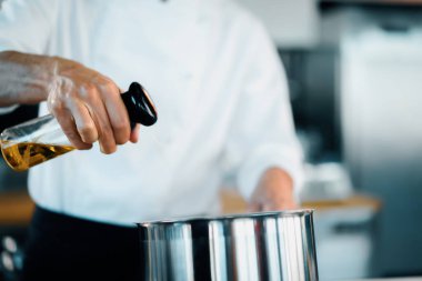 Professional restaurant kitchen, close-up: the chef splashes oil on pan