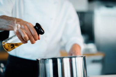 Professional restaurant kitchen, close-up: the chef splashes oil on pan
