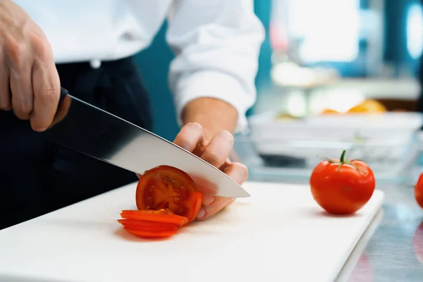 Close-up of chef slicing tomato in a professional restaurant kitchen