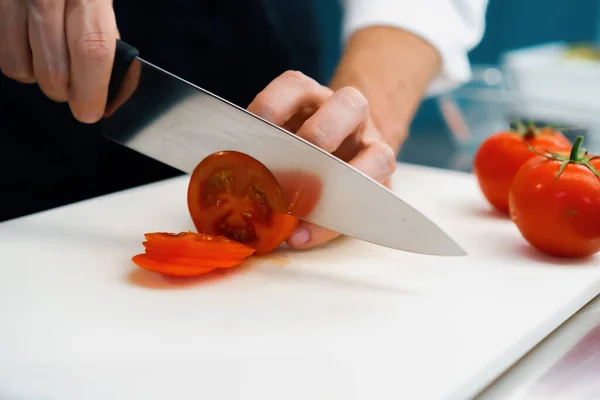 Close-up of chef slicing tomato in a professional restaurant kitchen