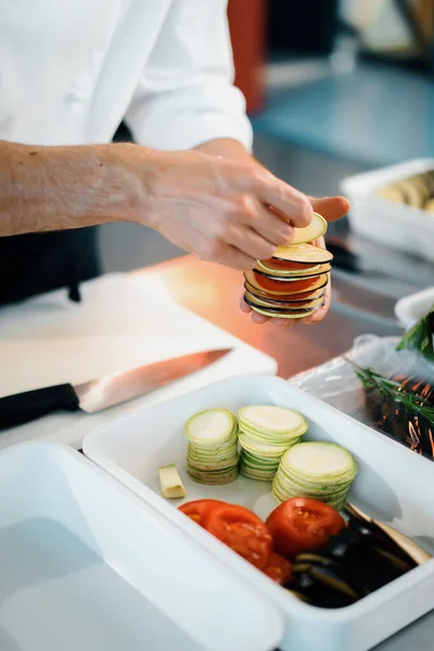Professional kitchen of the restaurant, close-up: chef collects ratatouille from vegetables