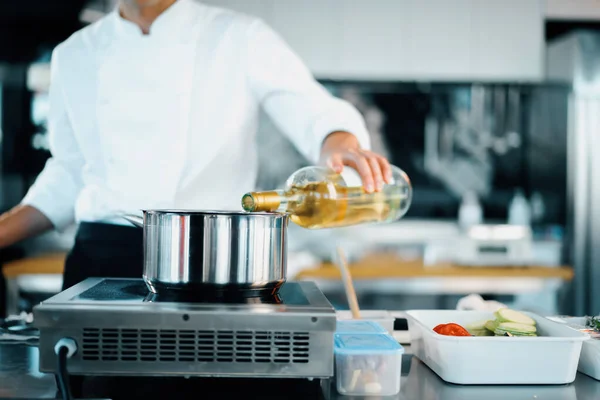 Professional kitchen of the restaurant, close-up: the chef pours wine into the pan while preparing delicious dish