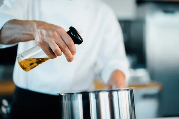 Professional restaurant kitchen, close-up: the chef splashes oil on pan