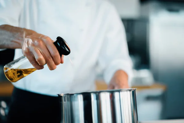 Professional restaurant kitchen, close-up: the chef splashes oil on pan