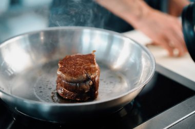 Professional restaurant kitchen, close-up: male chef preparing filet mignon on frying pan
