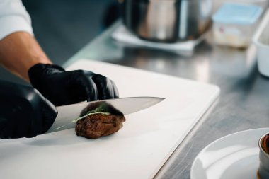 Professional kitchen of a restaurant, close-up: male chef cuts a ready-made delicious filet mignon