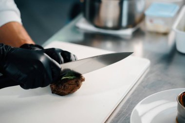 Professional kitchen of a restaurant, close-up: male chef cuts a ready-made delicious filet mignon