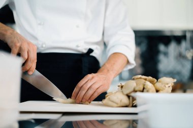 Professional kitchen: two chefs prepare food. The cook cuts mushrooms to prepare delicious dish.