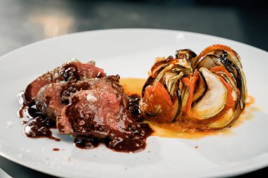 Professional restaurant kitchen, close-up: sliced delicious juicy filet mignon steak and the ratatouille