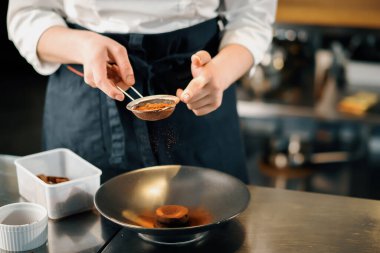 Professional restaurant kitchen, close up: female chef sprinkles brownies with chocolate and cinnamon