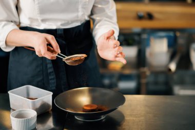 Professional restaurant kitchen, close up: female chef sprinkles brownies with chocolate and cinnamon