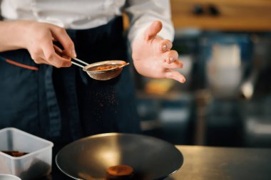 Professional restaurant kitchen, close up: female chef sprinkles brownies with chocolate and cinnamon