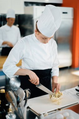 Professional restaurant kitchen, close-up: woman chef cuts mushrooms