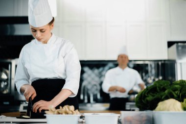 Professional restaurant kitchen, close-up: woman chef cuts mushrooms
