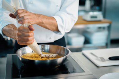 Professional kitchen of a restaurant, close-up: a male chef prepares french omelette in a frying pan