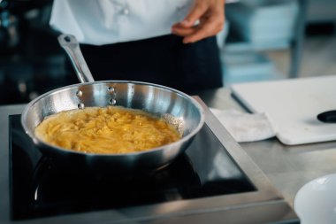 Professional kitchen of a restaurant, close-up: a male chef prepares french omelette in a frying pan