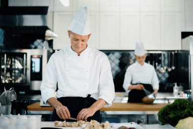 Professional kitchen: two chefs prepare food. The cook cuts mushrooms to prepare delicious dish.