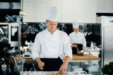Professional kitchen: chef prepare food. The cook cuts mushrooms to prepare delicious dish.
