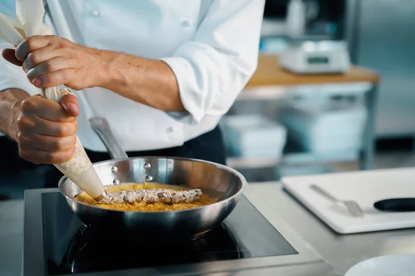 Professional kitchen of a restaurant, close-up: a male chef prepares french omelette in a frying pan