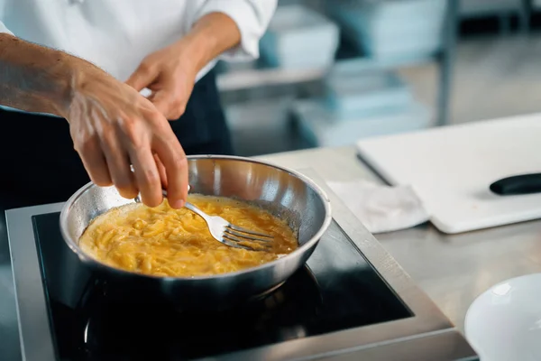 Professional kitchen of a restaurant, close-up: a male chef prepares french omelette in a frying pan