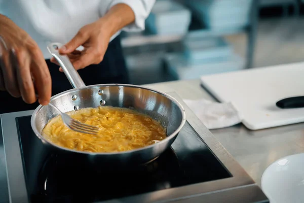 Professional kitchen of a restaurant, close-up: a male chef prepares french omelette in a frying pan
