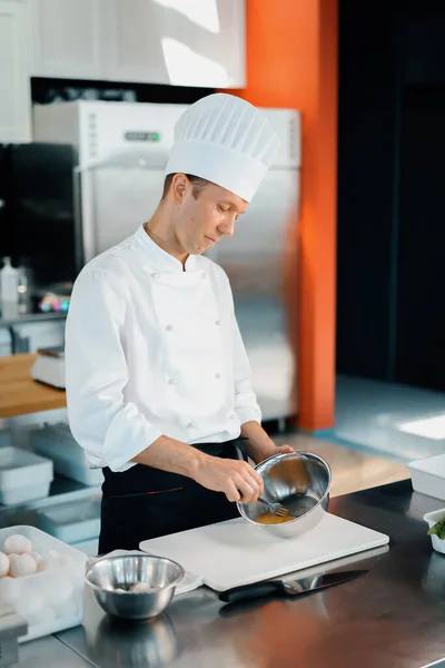 Restaurant professional kitchen: chef prepares delicious dish, beats eggs in a bowl