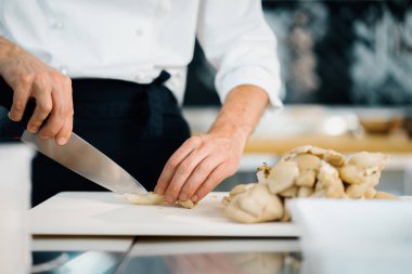 Professional kitchen: two chefs prepare food. The cook cuts mushrooms to prepare delicious dish.