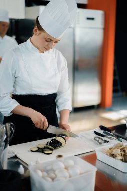 Professional restaurant kitchen, woman chef cuts a zucchini