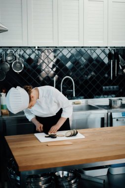 Professional restaurant kitchen, close-up: woman chef cuts mushrooms