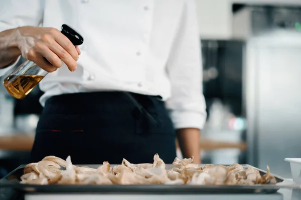 Professional restaurant kitchen, male chef splashes oil on mushrooms. Cooking delicious food in restaurant.