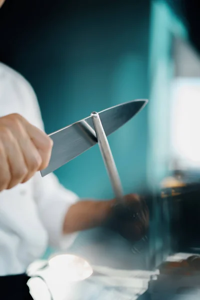 Professional restaurant kitchen, male chef sharpening knife