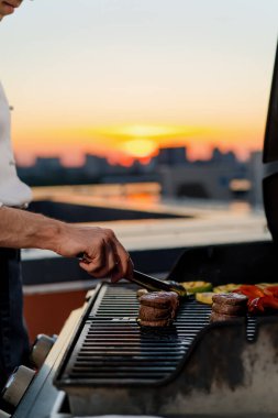 Close-up of filet mignon vegetables and meat on a bbq grill on skyscraper rooftop at sunset. Fire in the barbecue