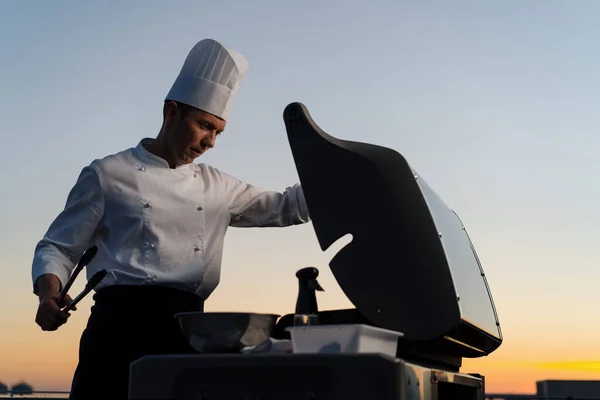Skyscraper Rooftop: A professional male chef prepares barbecue at a party or outdoor restaurant. Grilled meat, vegetable