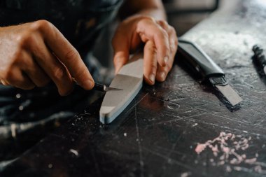 Close-up: artisan sculptor artist sharpening blade on a sharpener in a workshop