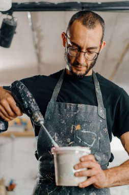 Artisan artist mixing paint in his workshop. Pink paint, paint mixer