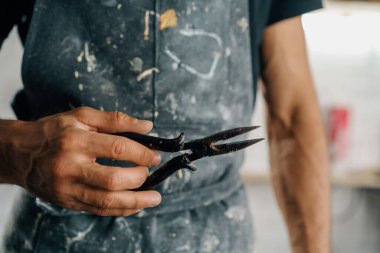 Male artist sculptor artisan works with tongs in workshop