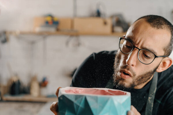 Close-up: male artist sculptor artisan blows dust off an item. Handmade workshop.