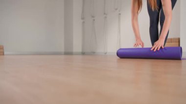 Woman spreading yoga mat after training in studio. Girl folding fitness mat on floor at yoga studio