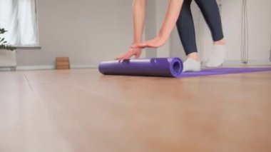 Woman spreading yoga mat after training in studio. Girl folding fitness mat on floor at yoga studio