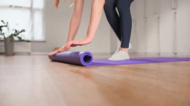 Woman rolling up yoga mat after training in studio. Girl folding fitness mat on floor at yoga studio