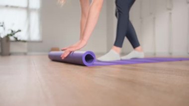 Woman rolling up yoga mat after training in studio. Girl folding fitness mat on floor at yoga studio