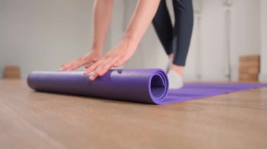 Woman rolling up yoga mat after training in studio. Girl folding fitness mat on floor at yoga studio