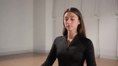 Relaxed young woman is meditating in lotus position sitting on yoga mat with closed eyes and hands in namaste