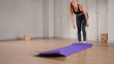 Woman rolling up yoga mat after training in studio. Girl folding fitness mat on floor at yoga studio