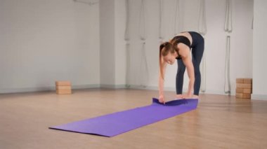 Woman rolling up yoga mat after training in studio. Girl folding fitness mat on floor at yoga studio
