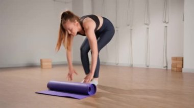 Woman spreading yoga mat after training in studio. Girl folding fitness mat on floor at yoga studio