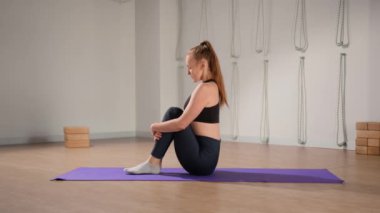 Determined athletic woman exercising, stretching exercises on yoga mat while watching online fitness course video on tablet. Woman practicing yoga online with laptop