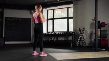 Attractive young beautiful woman doing cardio exercise and squatting with kettlebell in gym