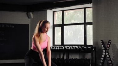 Attractive young beautiful woman doing cardio exercise and squatting with kettlebell in gym